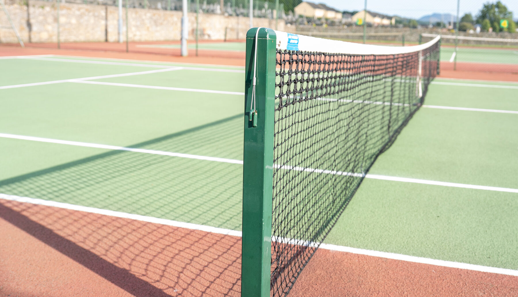 The club courts on a clear summer afternoon, net post in the foreground